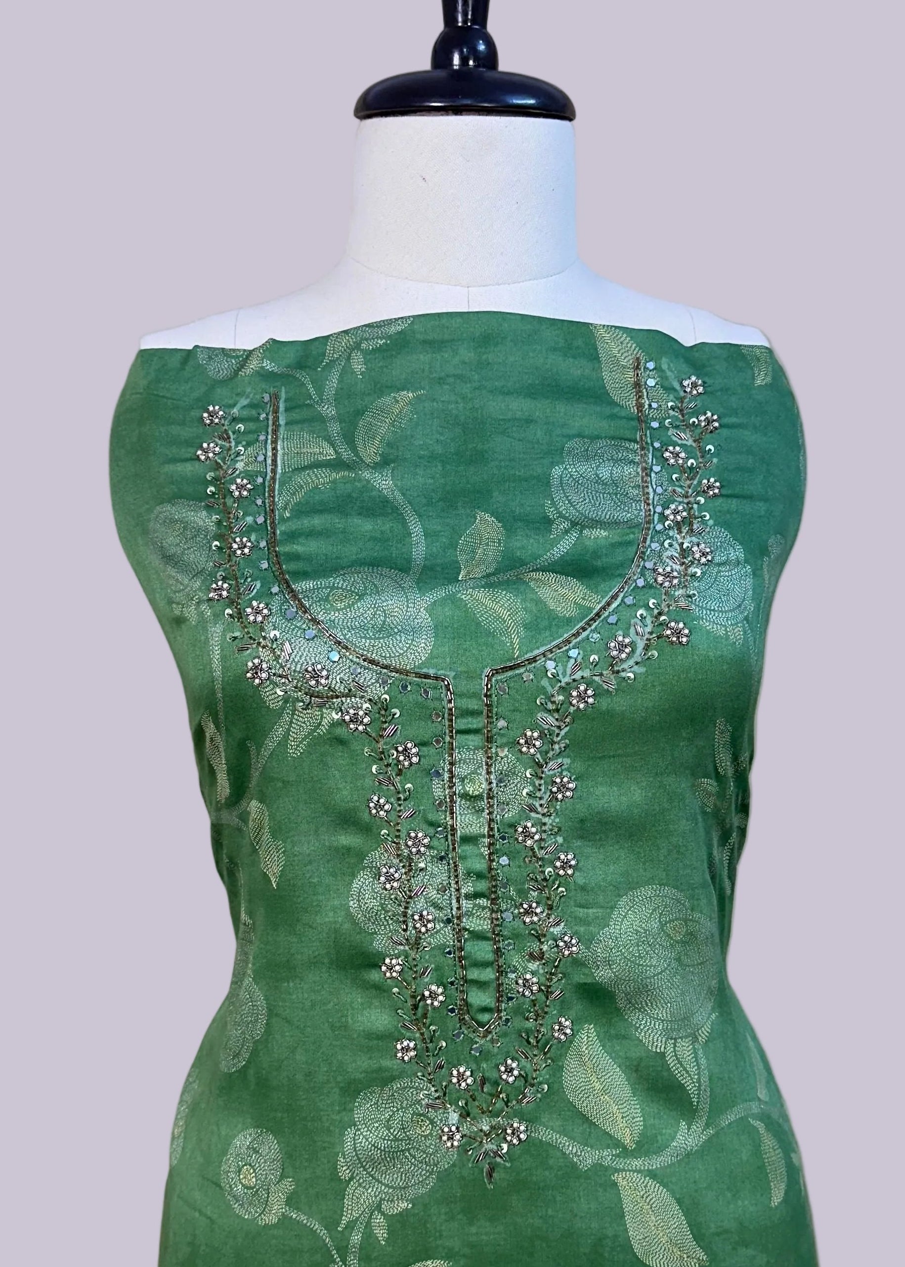 Green dress with floral patterns and embellishments on a mannequin against a plain background