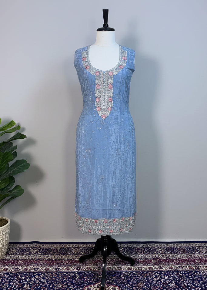 Mannequin wearing a light blue embroidered outfit on a patterned rug with a beige curtain background