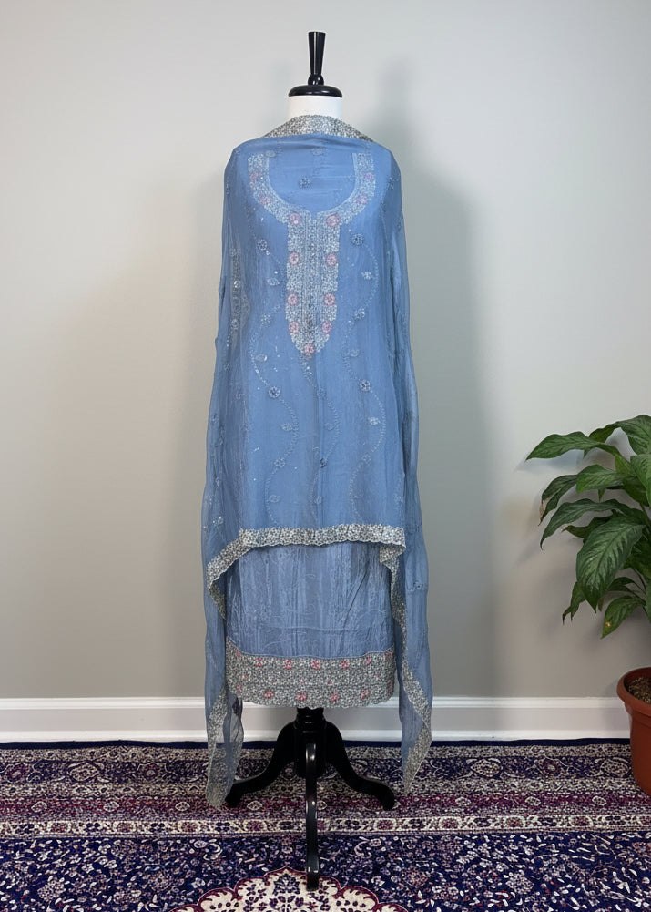 Blue embroidered traditional outfit on a mannequin against a beige curtain.