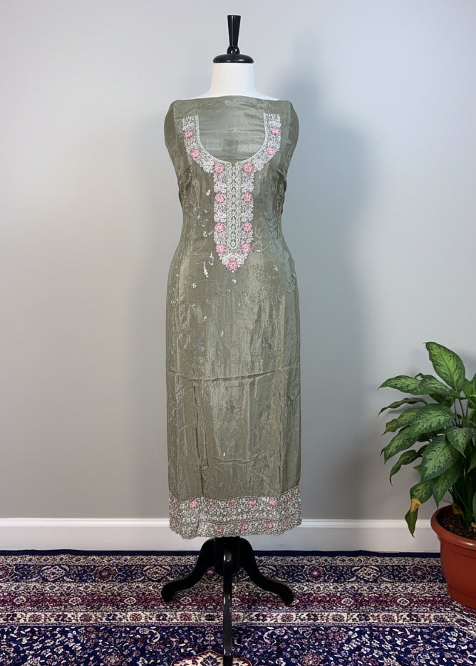 Green dress with intricate patterns on a mannequin against a beige curtain background