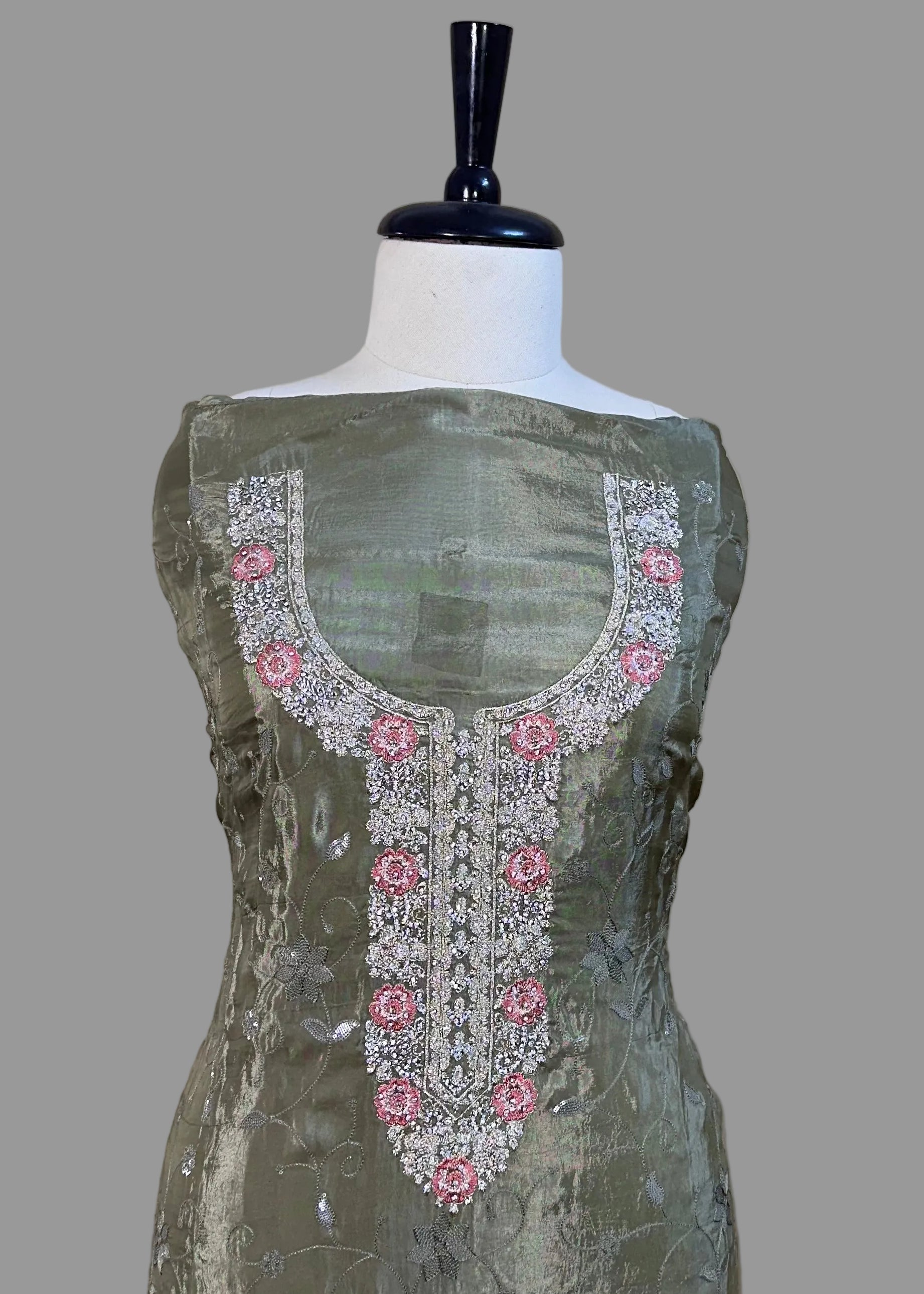 Green embroidered dress on a mannequin against a beige curtain background