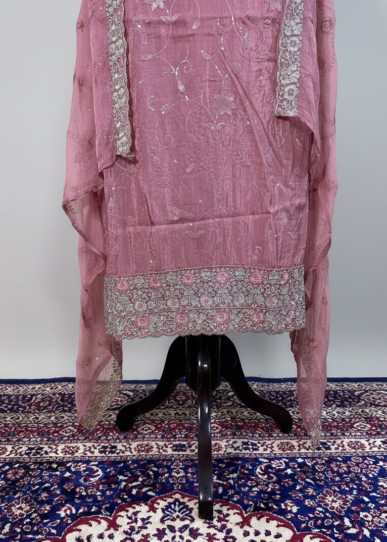 Pink embroidered traditional outfit on a black stand against a patterned rug