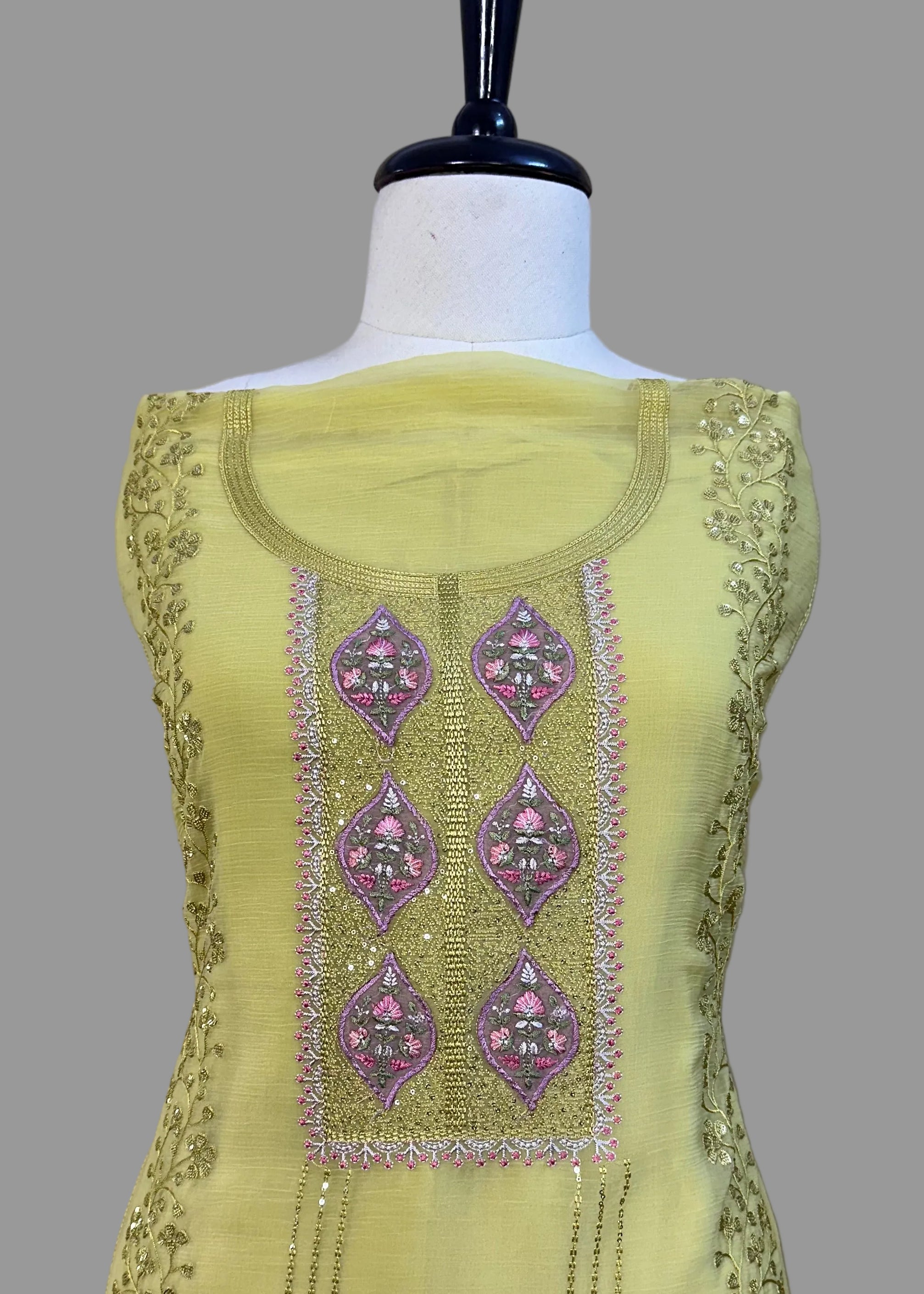 Light green dress with intricate purple embroidery on a mannequin against a neutral background