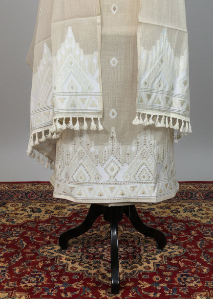 Beige embroidered traditional outfit on a stand with a patterned rug and chair in the background