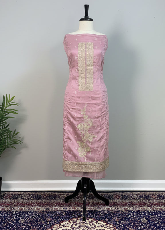 Pink dress on a mannequin against a beige curtain with a patterned rug below