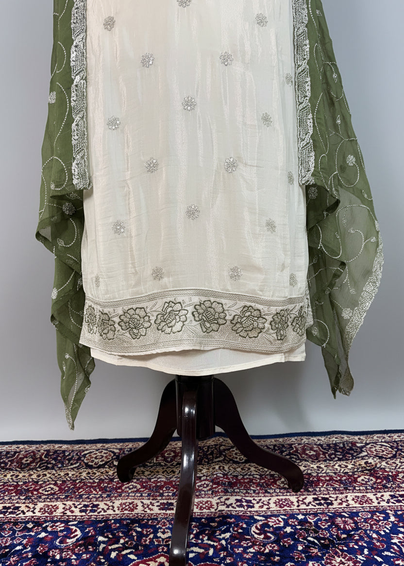 White embroidered outfit with green dupatta on a mannequin against a patterned rug.