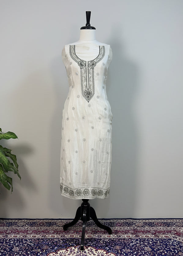White dress with black embroidery on a mannequin against a beige curtain background.