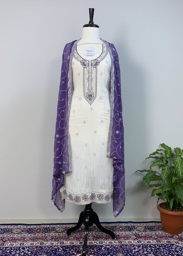 Mannequin wearing a white dress with purple accents on a patterned rug.