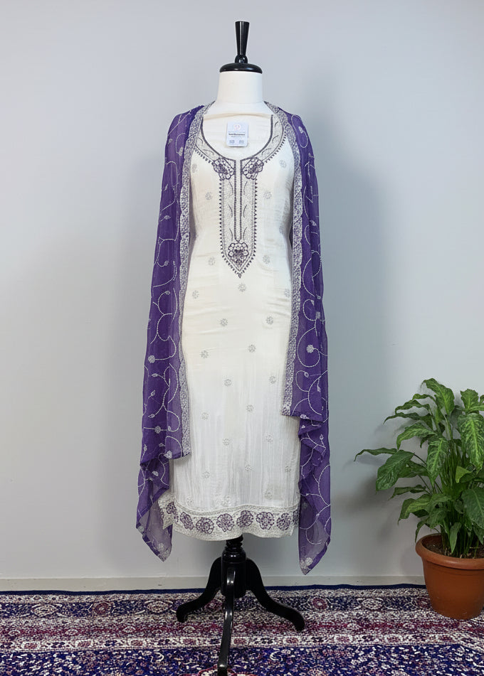 Mannequin wearing a white dress with purple accents on a patterned rug.