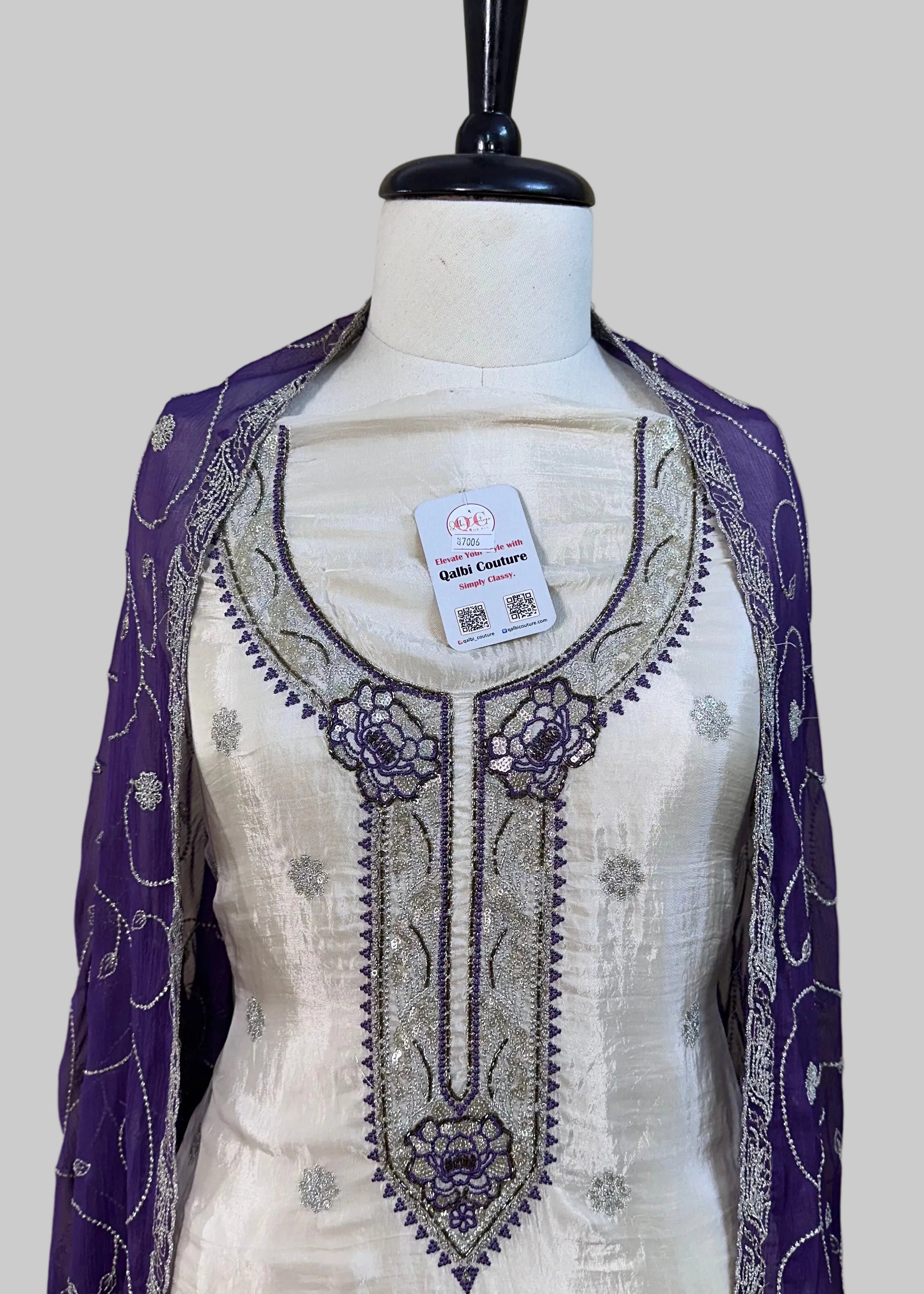 White embroidered dress with purple accents on a mannequin against a neutral background