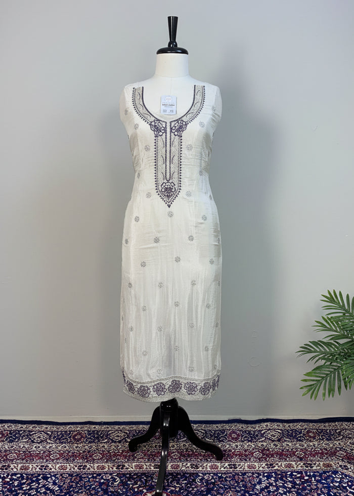 White dress with black embroidery on a mannequin against a beige curtain background.