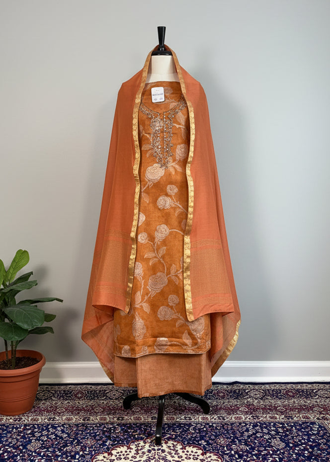 Brown traditional outfit with floral patterns on a mannequin against a beige curtain.