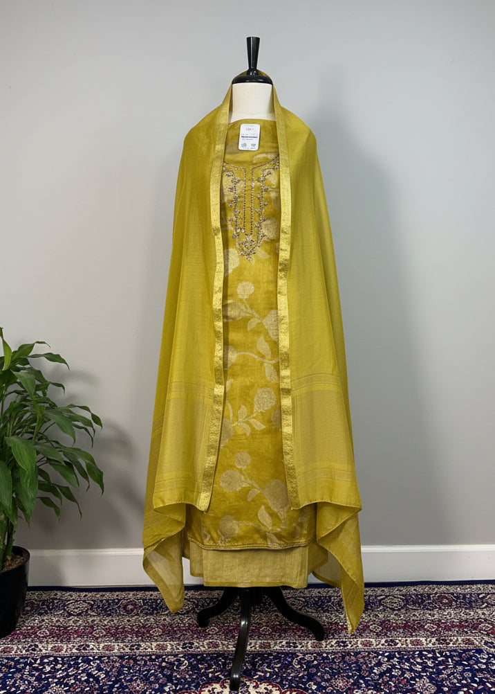 Green embroidered outfit on a mannequin against a beige curtain background