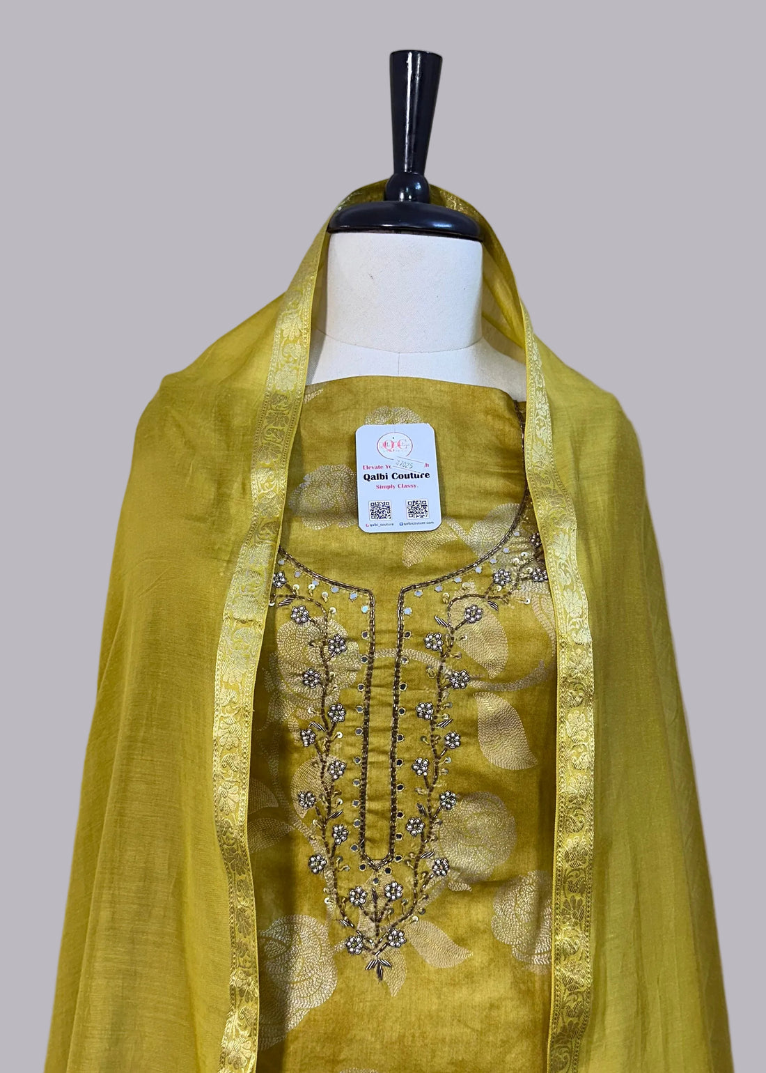 Green embroidered outfit on a mannequin against a beige curtain background