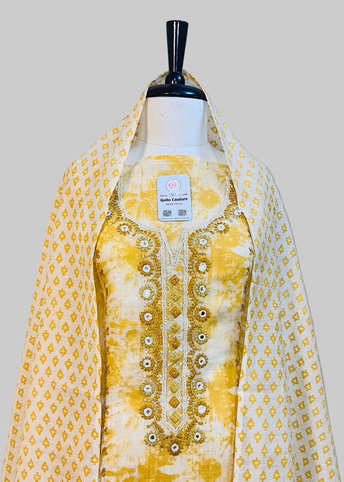 Yellow and white embroidered traditional outfit on a mannequin against a plain background