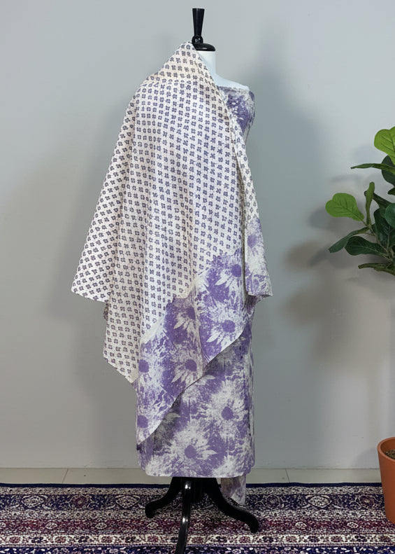 Mannequin wearing a white and purple patterned dress against a beige curtain.