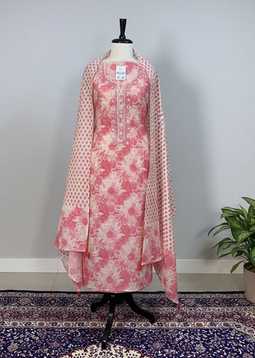 Mannequin wearing a pink floral outfit with a matching dupatta against a beige curtain background.