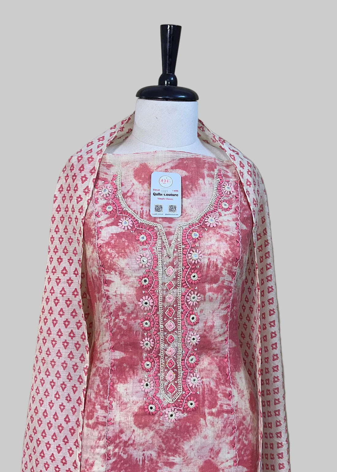 Mannequin wearing a pink floral outfit with a matching dupatta against a beige curtain background.