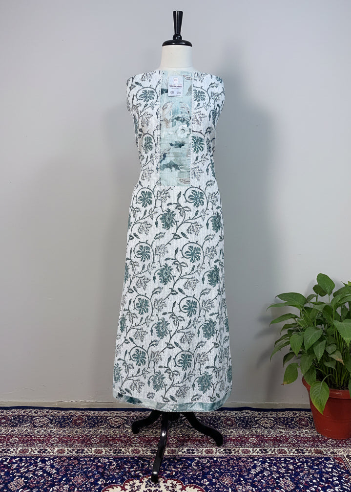 White dress with black floral pattern on a mannequin against a beige curtain.