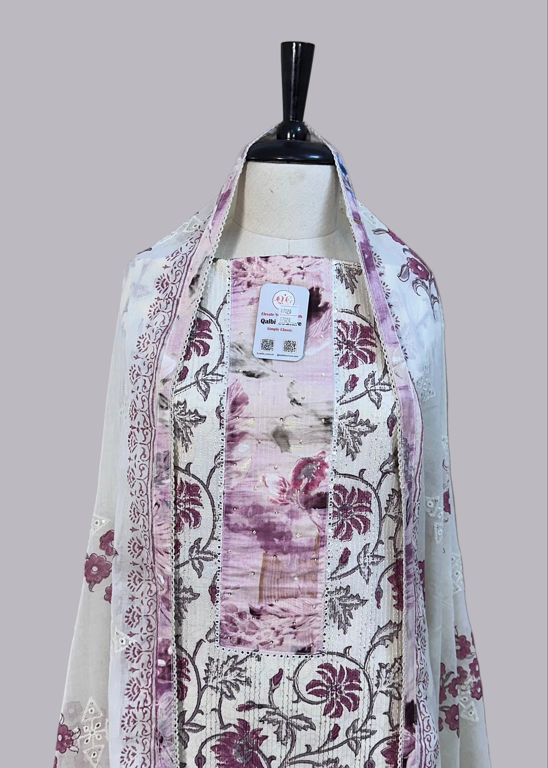 Floral dress on a mannequin against a beige curtain with a patterned rug below.