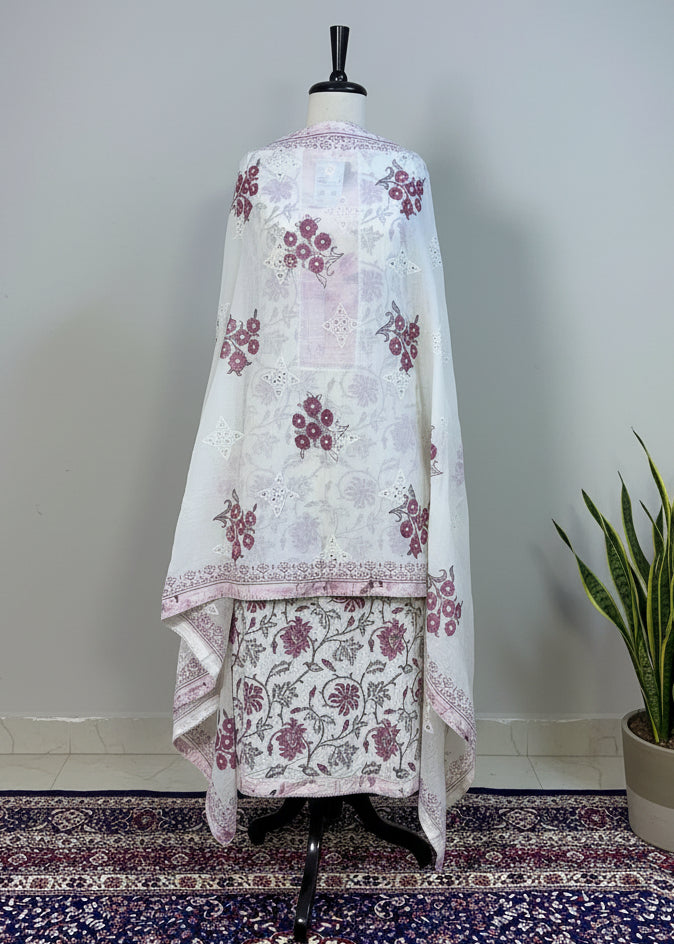 White traditional outfit with purple floral patterns on a mannequin against a beige curtain.