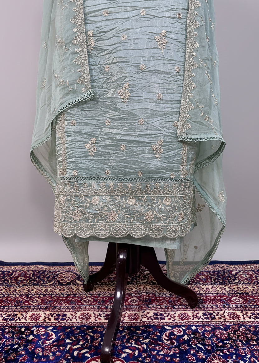 Light blue embroidered traditional outfit on a stand with a patterned rug below