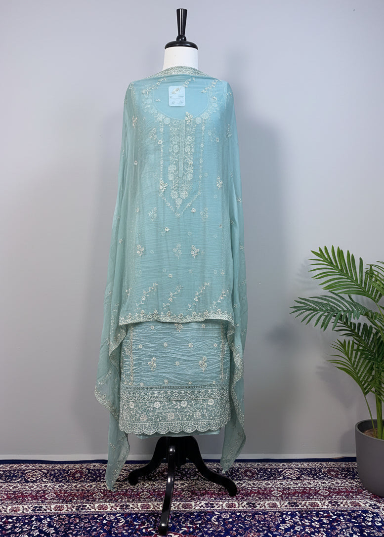 Teal embroidered outfit on a mannequin against a beige curtain background