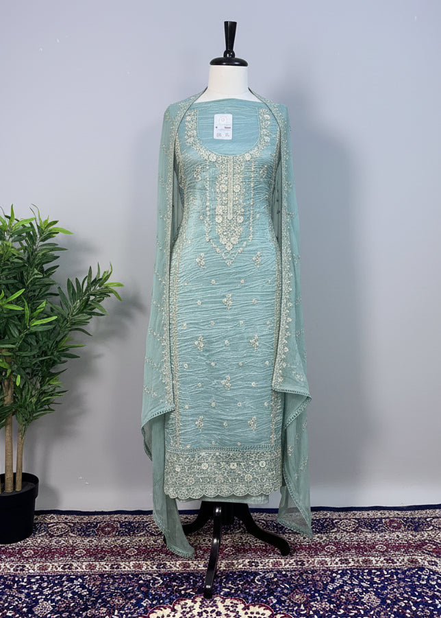 Teal embroidered dress on a mannequin against a beige curtain background