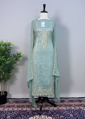 Teal embroidered dress on a mannequin against a beige curtain background