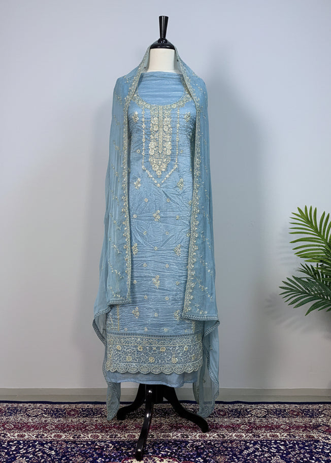 Light blue embroidered traditional outfit on a mannequin against a beige curtain background.
