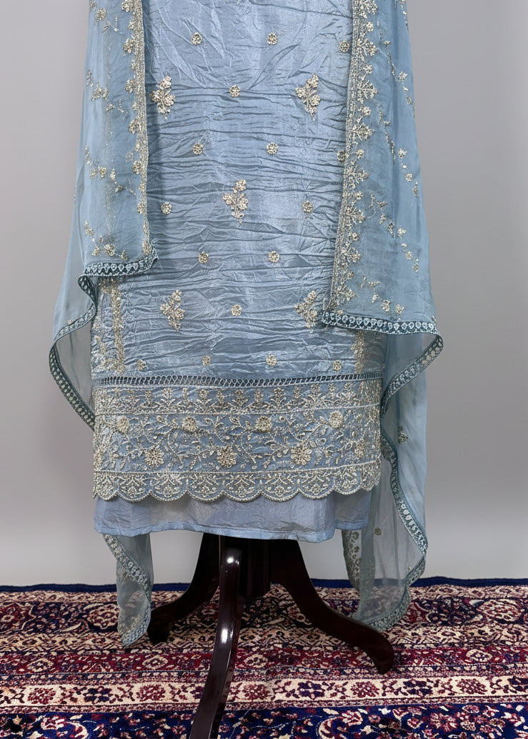 Light blue embroidered traditional outfit on a stand with a beige wall and patterned rug in the background