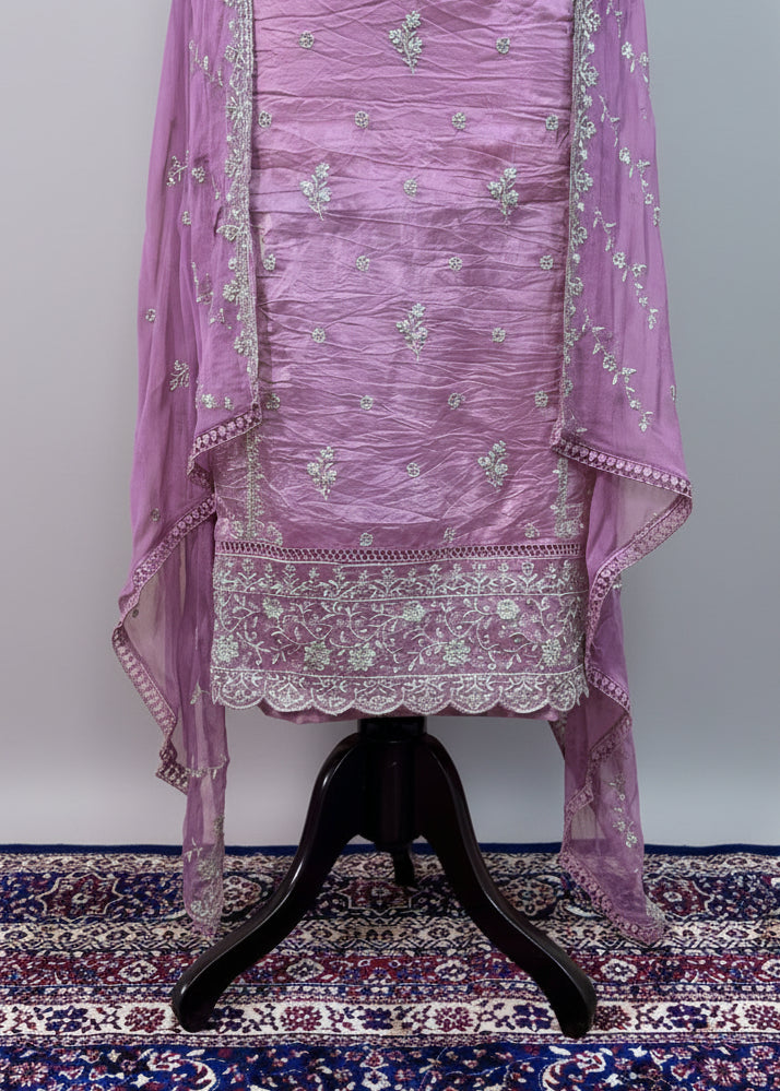 Purple embroidered traditional outfit on a stand with a white curtain background