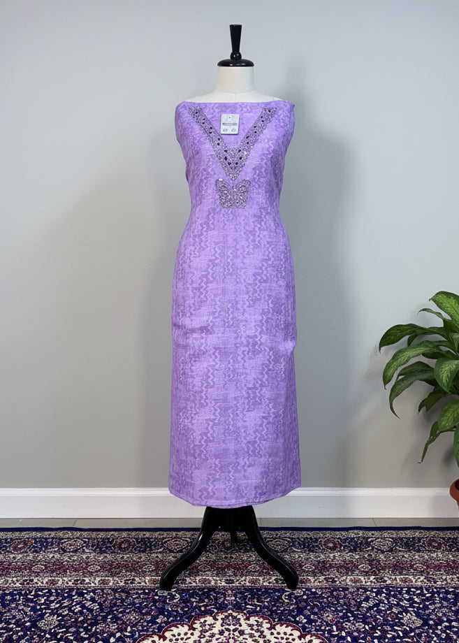 Purple dress on a mannequin against a beige curtain with a patterned rug below.