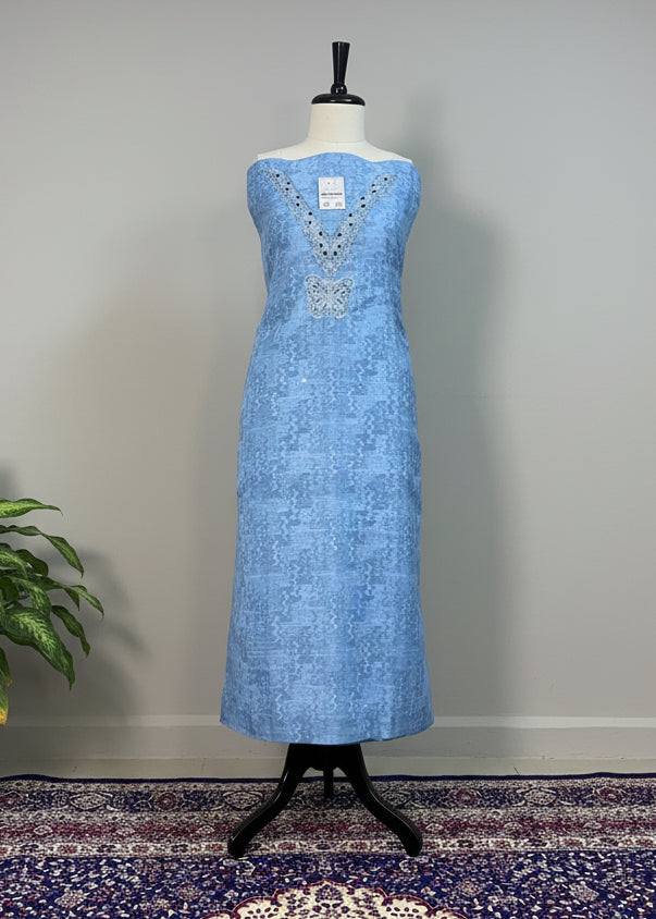 Blue dress on a mannequin against a beige curtain with a patterned rug below.