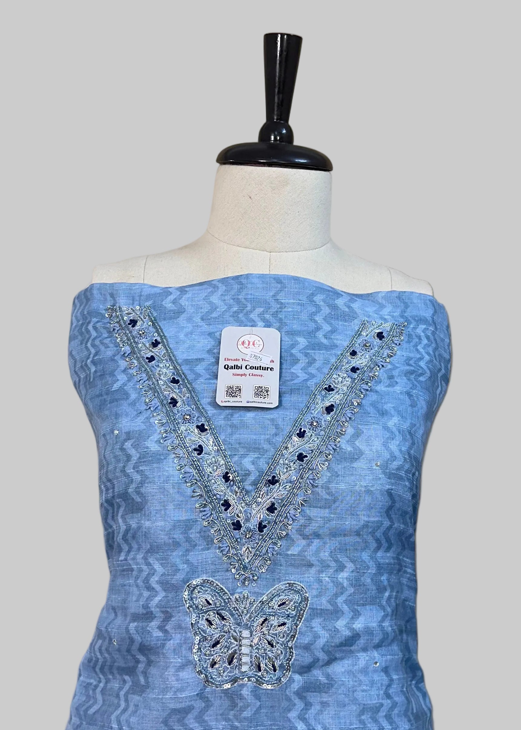 Blue dress with intricate designs on a mannequin against a beige background
