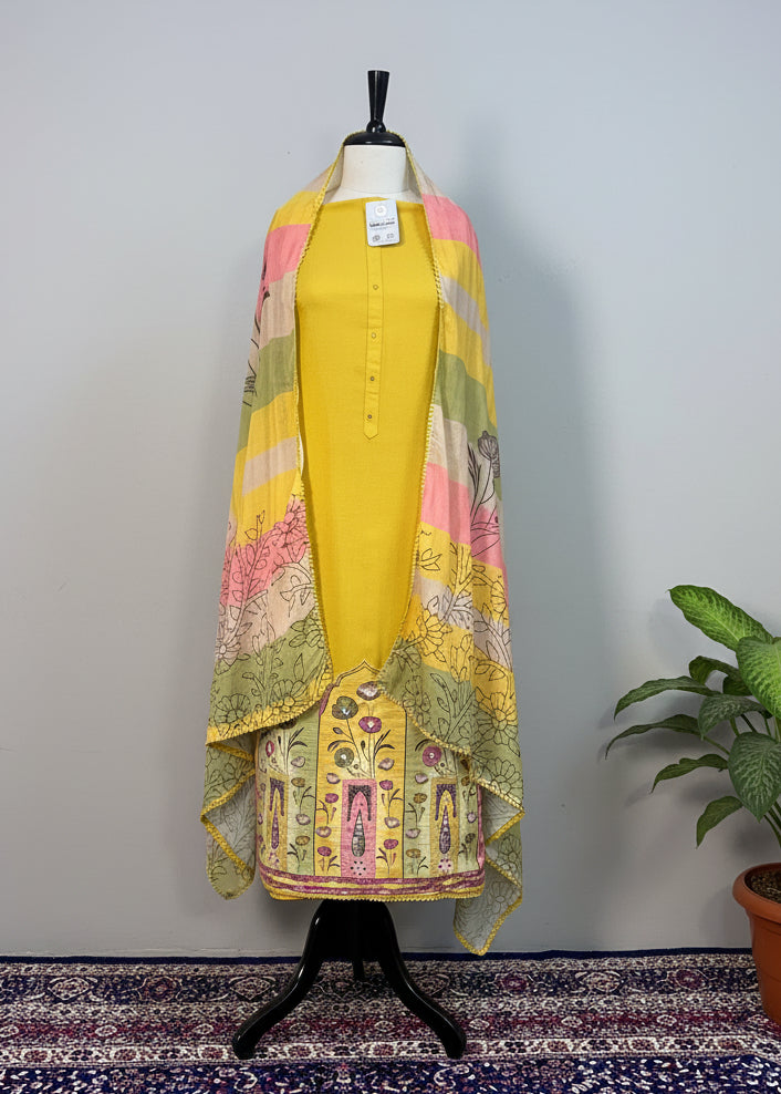 Mannequin wearing a yellow outfit with a colorful scarf against a beige curtain background