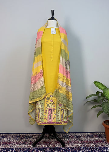 Mannequin wearing a yellow outfit with a colorful scarf against a beige curtain background