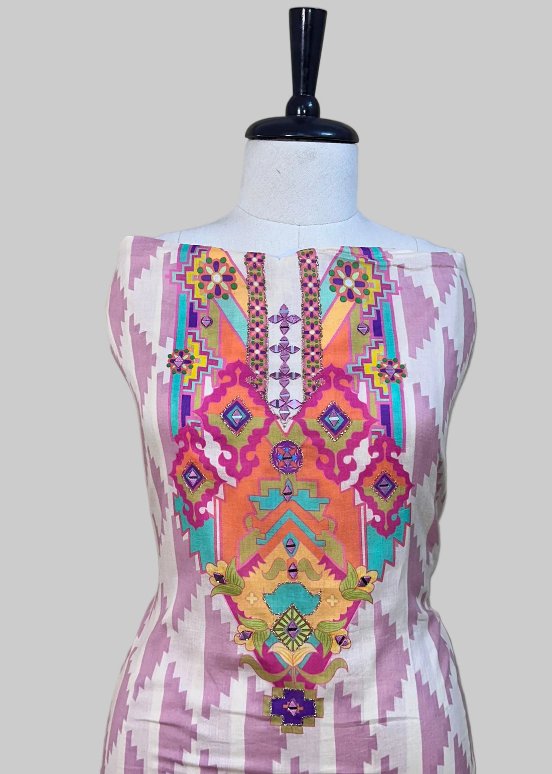 Mannequin wearing a colorful dress with an orange dupatta on a patterned rug.
